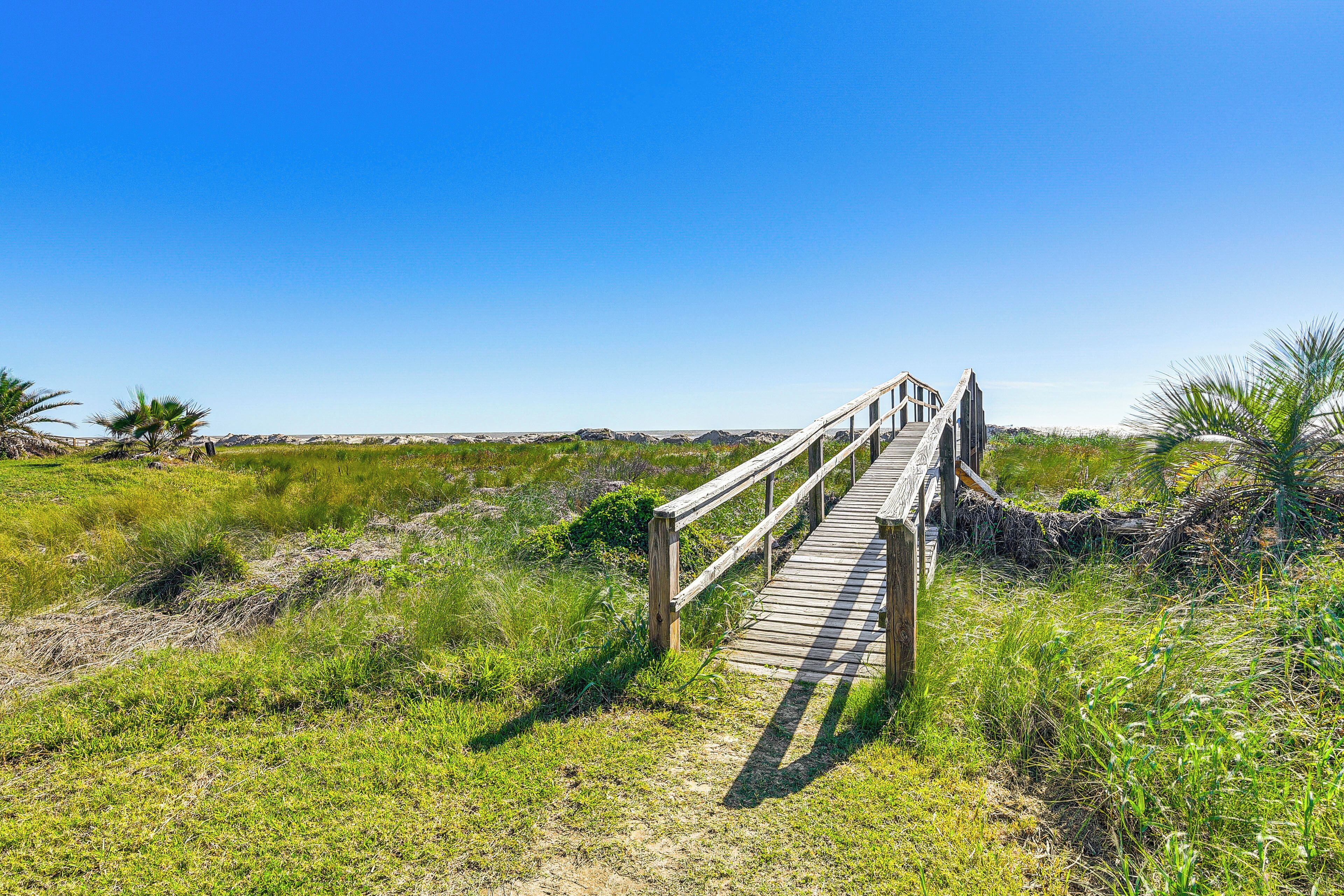 A wooden boardwalk leading to a beach with grassy dunes and sparse vegetation.