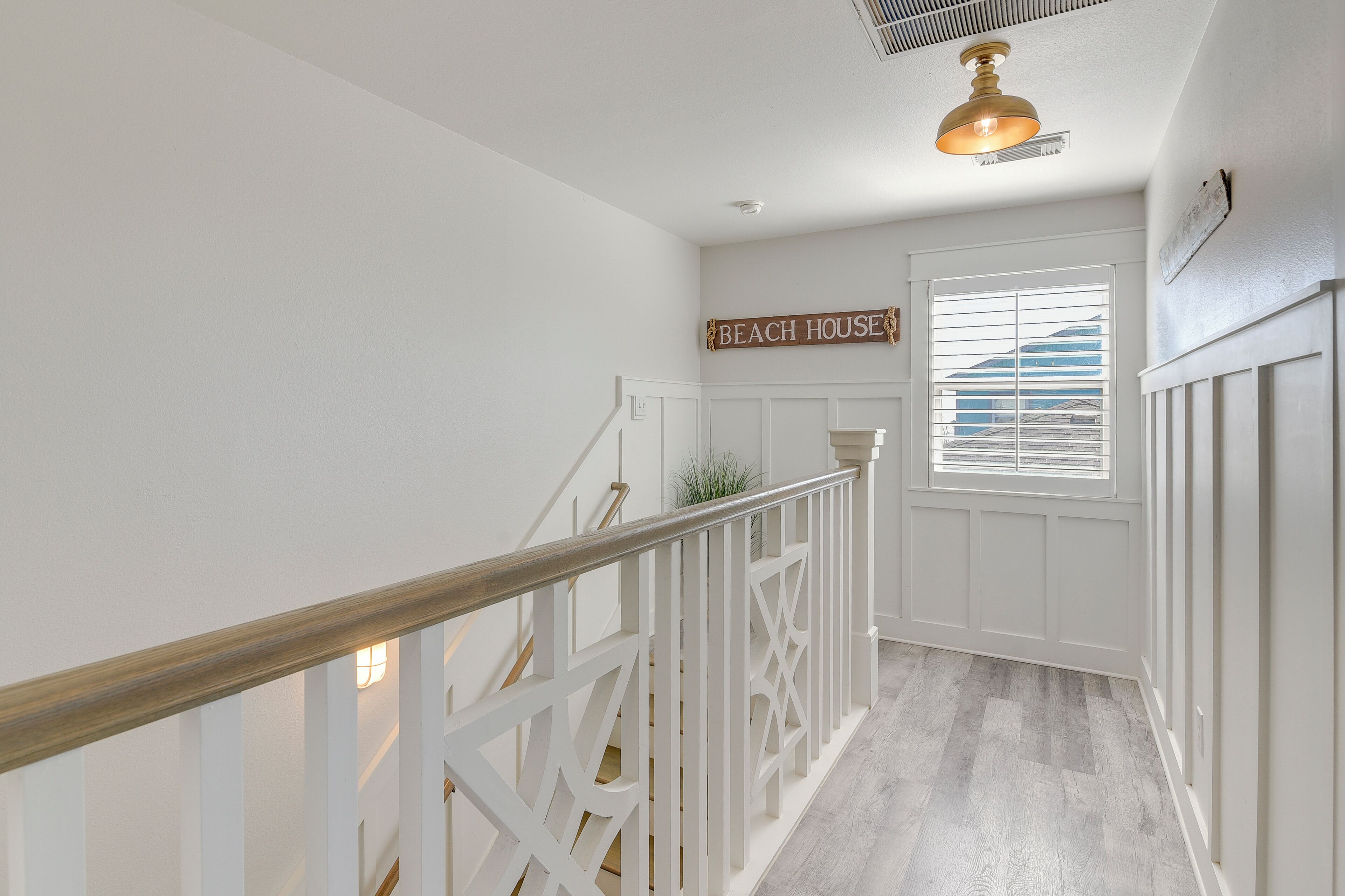 Un escalier avec des rampes blanches et une main courante en bois, menant à une porte sur laquelle est inscrit « MAISON DE PLAGE ».