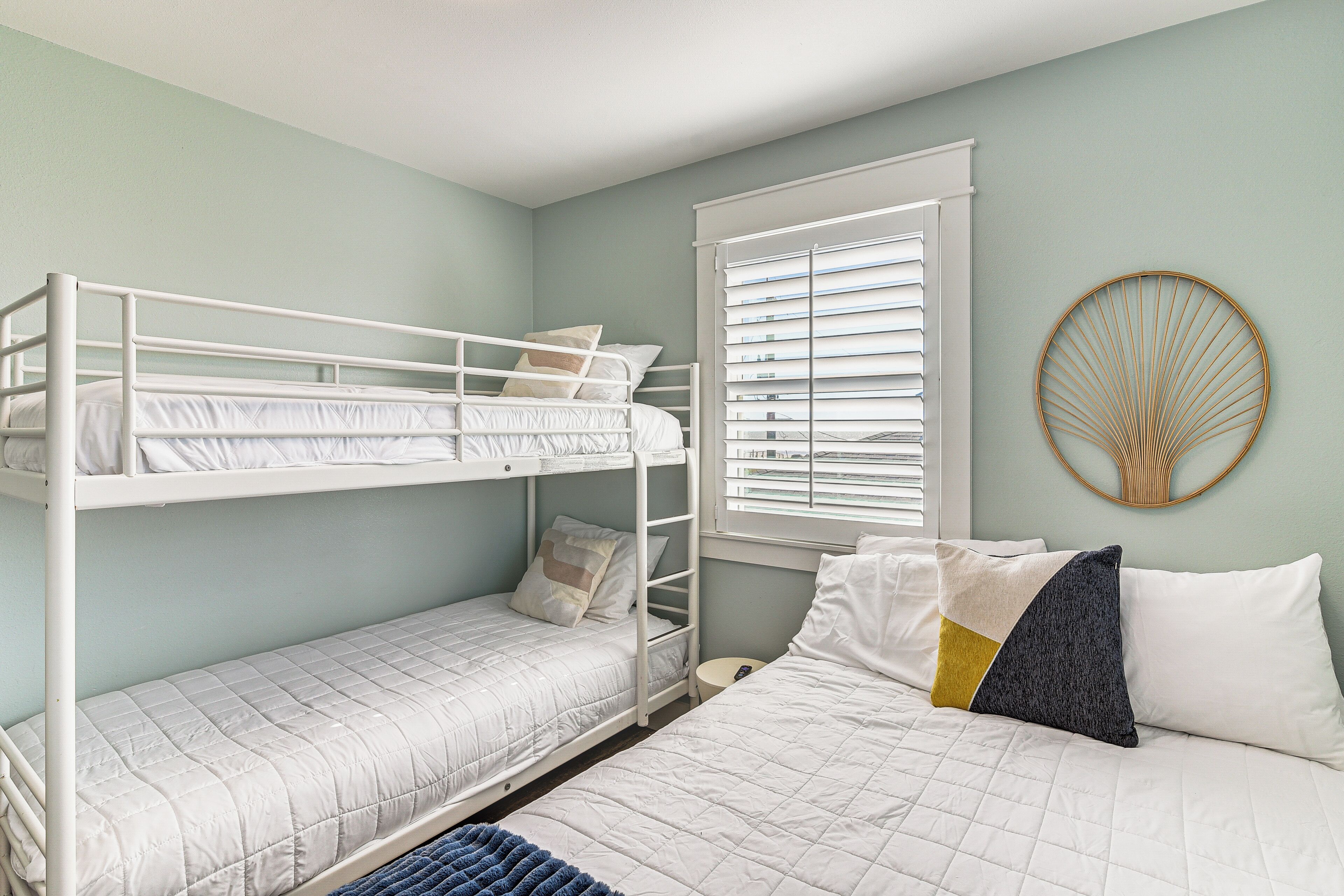 A room with bunk beds, a round wall decoration, and a window with blinds.