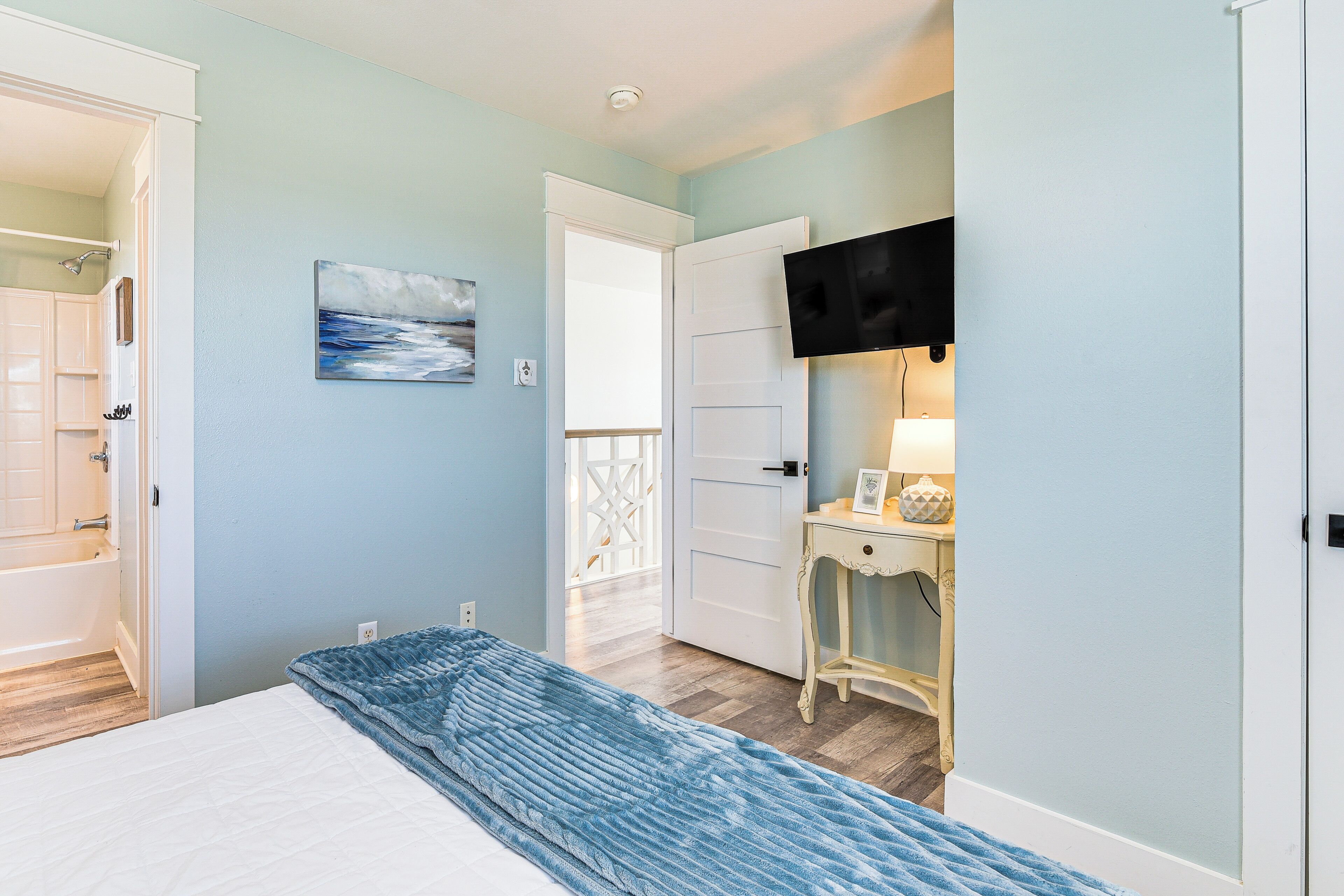 A bedroom with a bed, a painting, a TV, and a small table with a lamp.