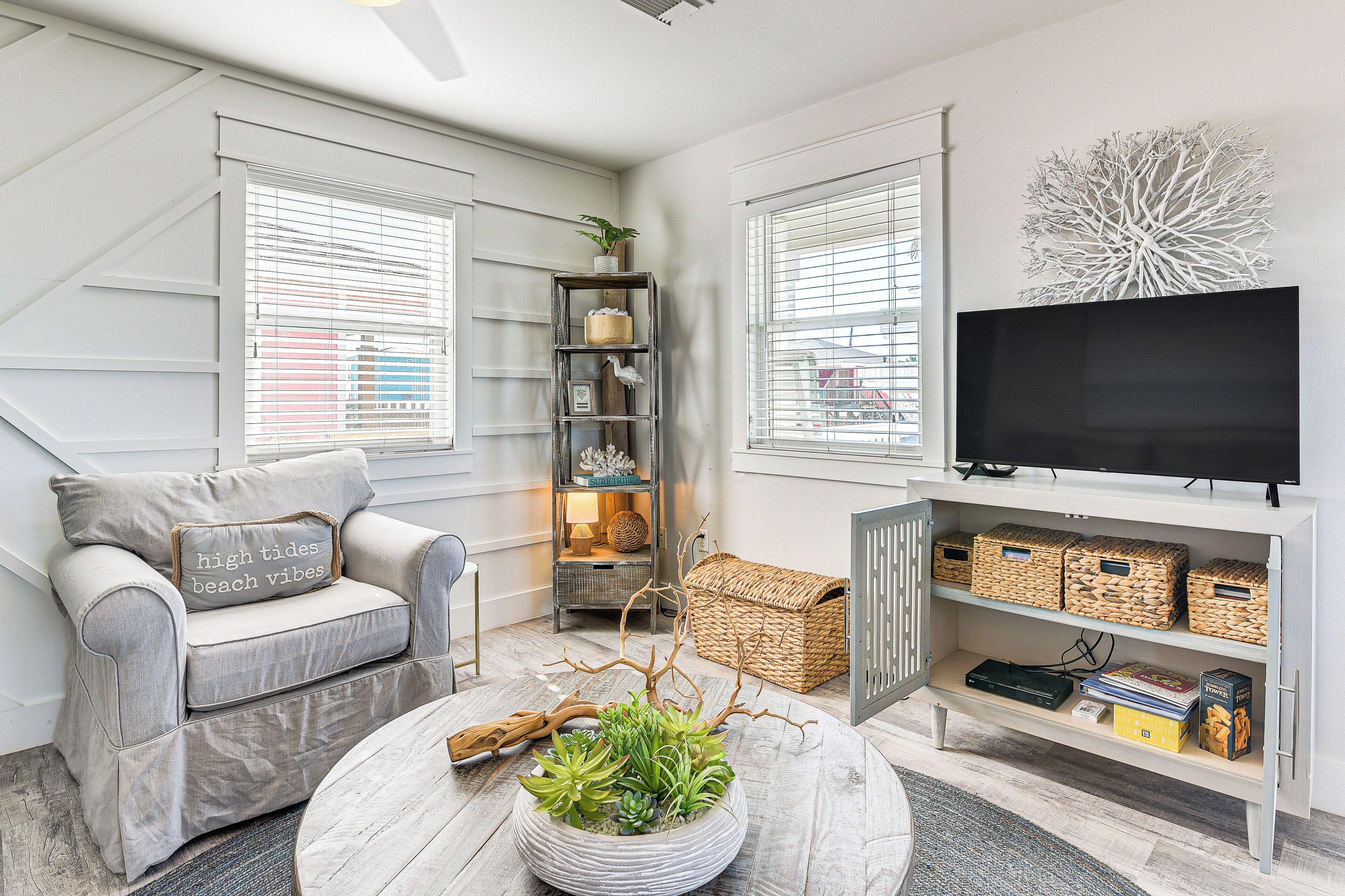 A modern living room with a grey sofa, a coffee table with a plant, a TV on a white stand, and a bookshelf.