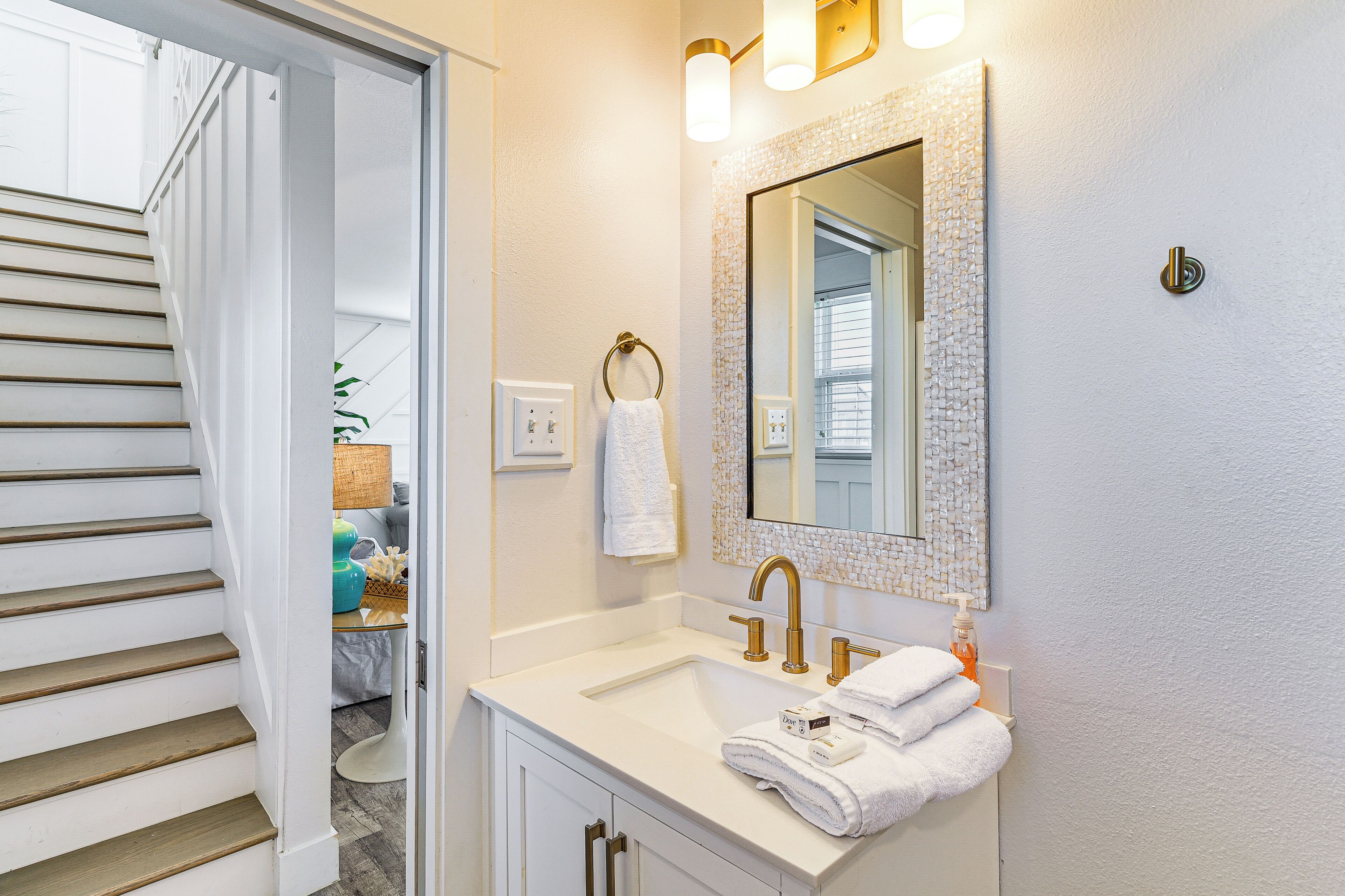 A bathroom with a white sink, gold faucets, and a mirror with a textured frame.