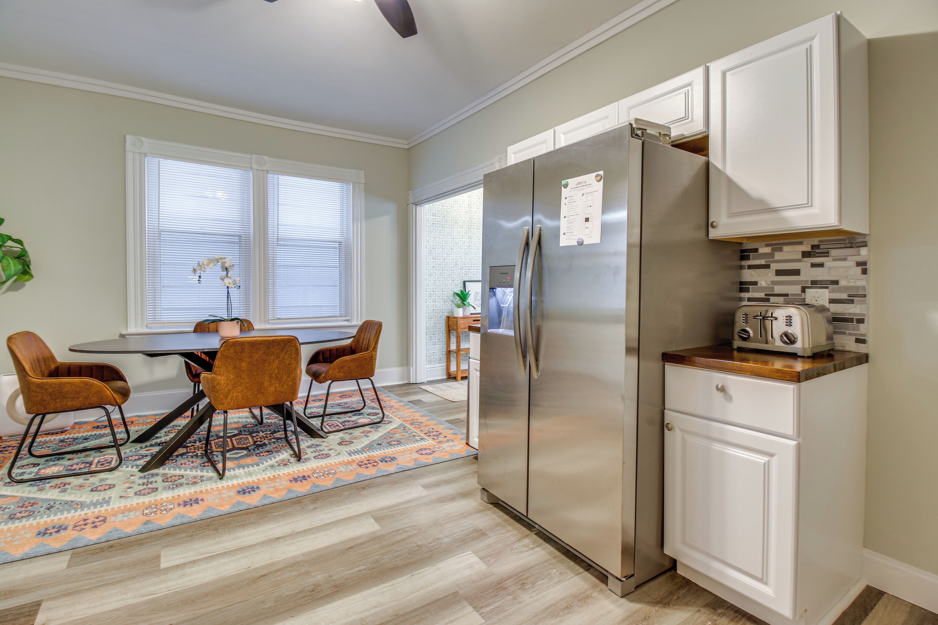 Una cocina moderna con armarios blancos, un refrigerador de acero inoxidable y un comedor con una mesa redonda y cuatro sillas.