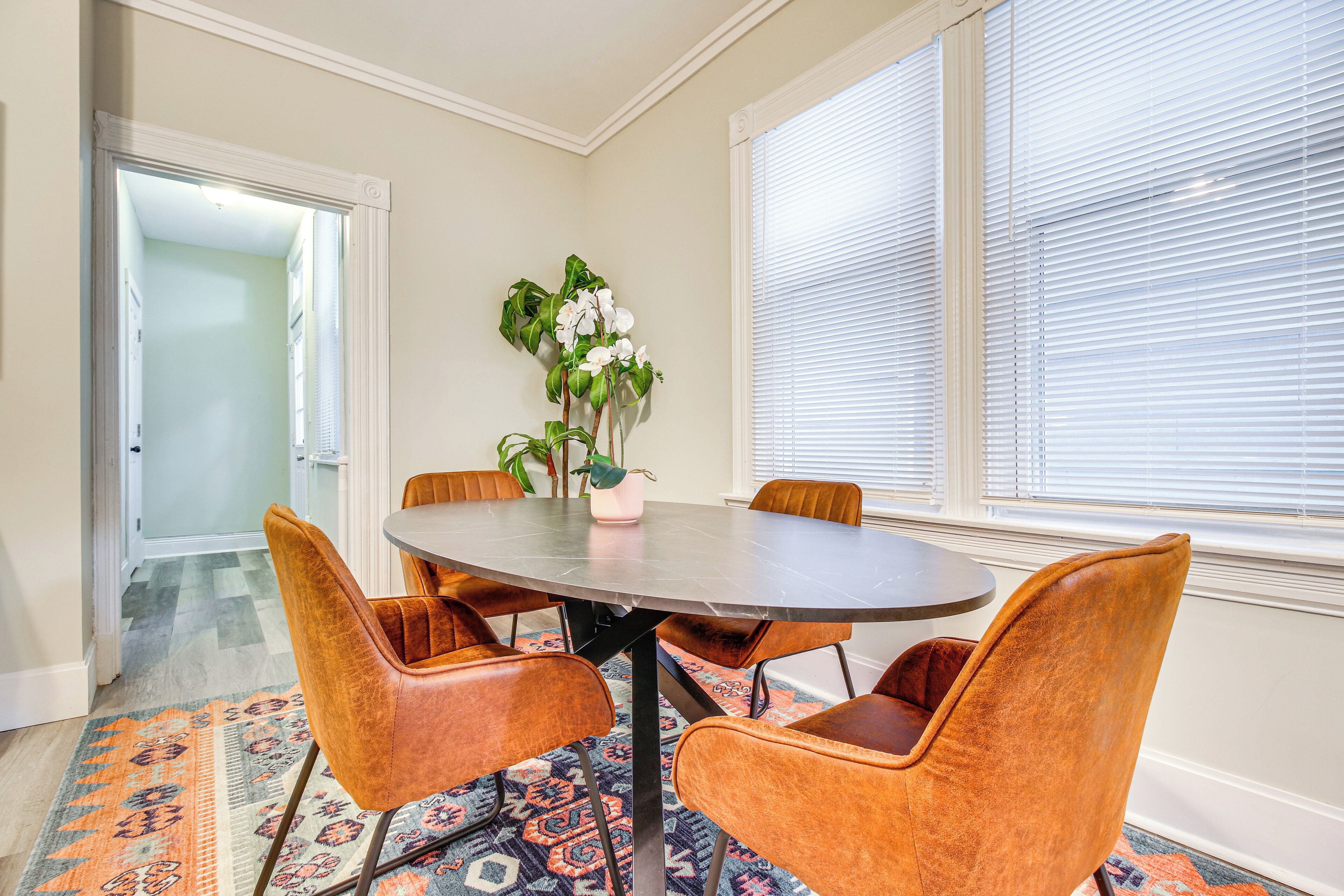 Een eethoek met een ronde tafel, vier stoelen, een potplant en een tapijt met patroon.
