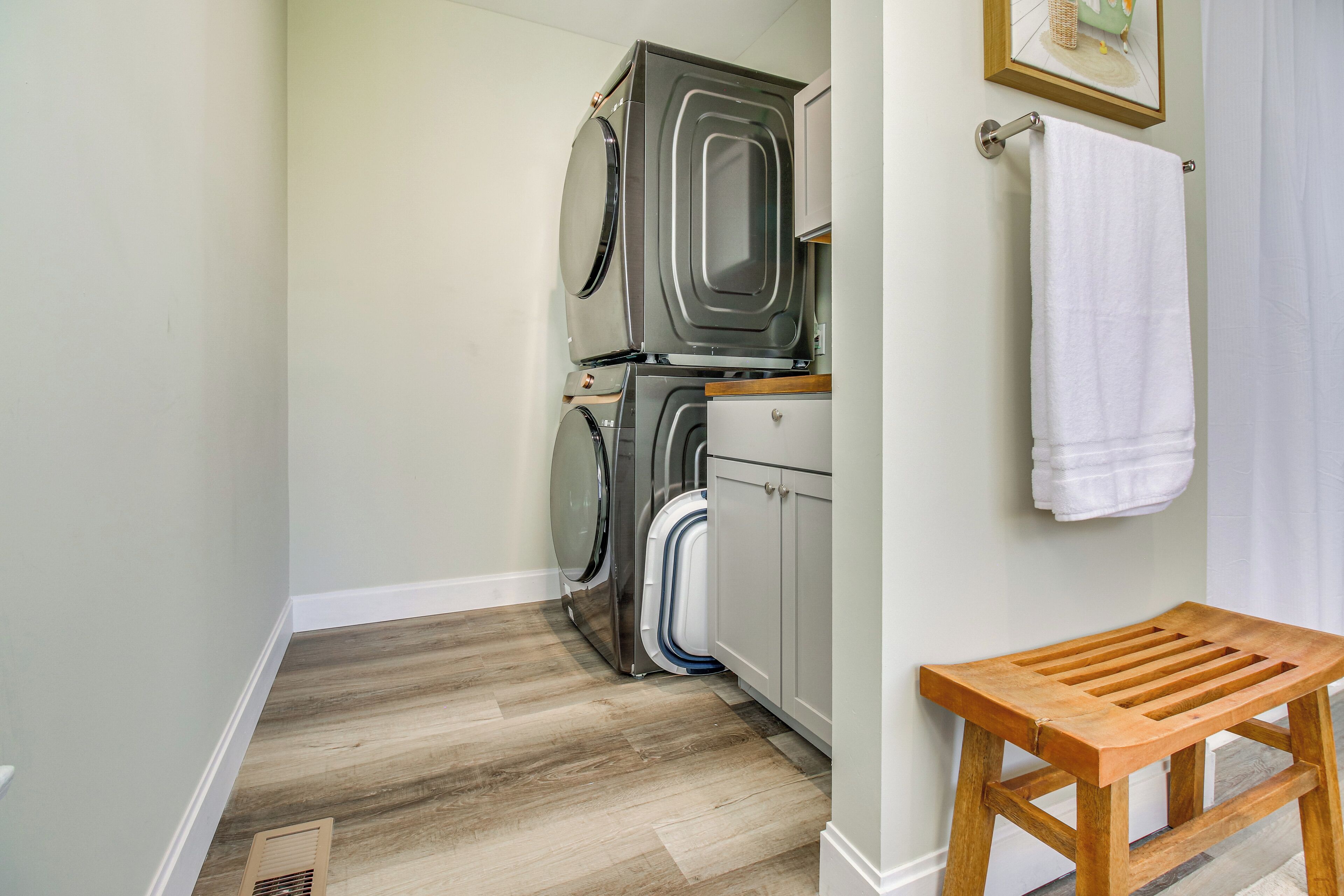 A laundry room with stacked washers and dryers, a wooden bench, and a towel hanging on a rack.