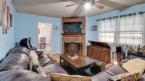 A living room with a sofa, coffee table, fireplace, TV, and artwork on the walls. - Near Fort Liberty: Home w/ Yard in Fayetteville! (Fayetteville)