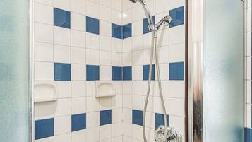 A shower area with blue and white tiles, a handheld showerhead, and a wall-mounted control.