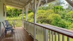 A covered porch with wooden railings and two chairs. The porch overlooks a lush garden with various plants and trees. - 4 Mi to Beach: Keaau Retreat w/ Relaxing Porch! (Keaau)