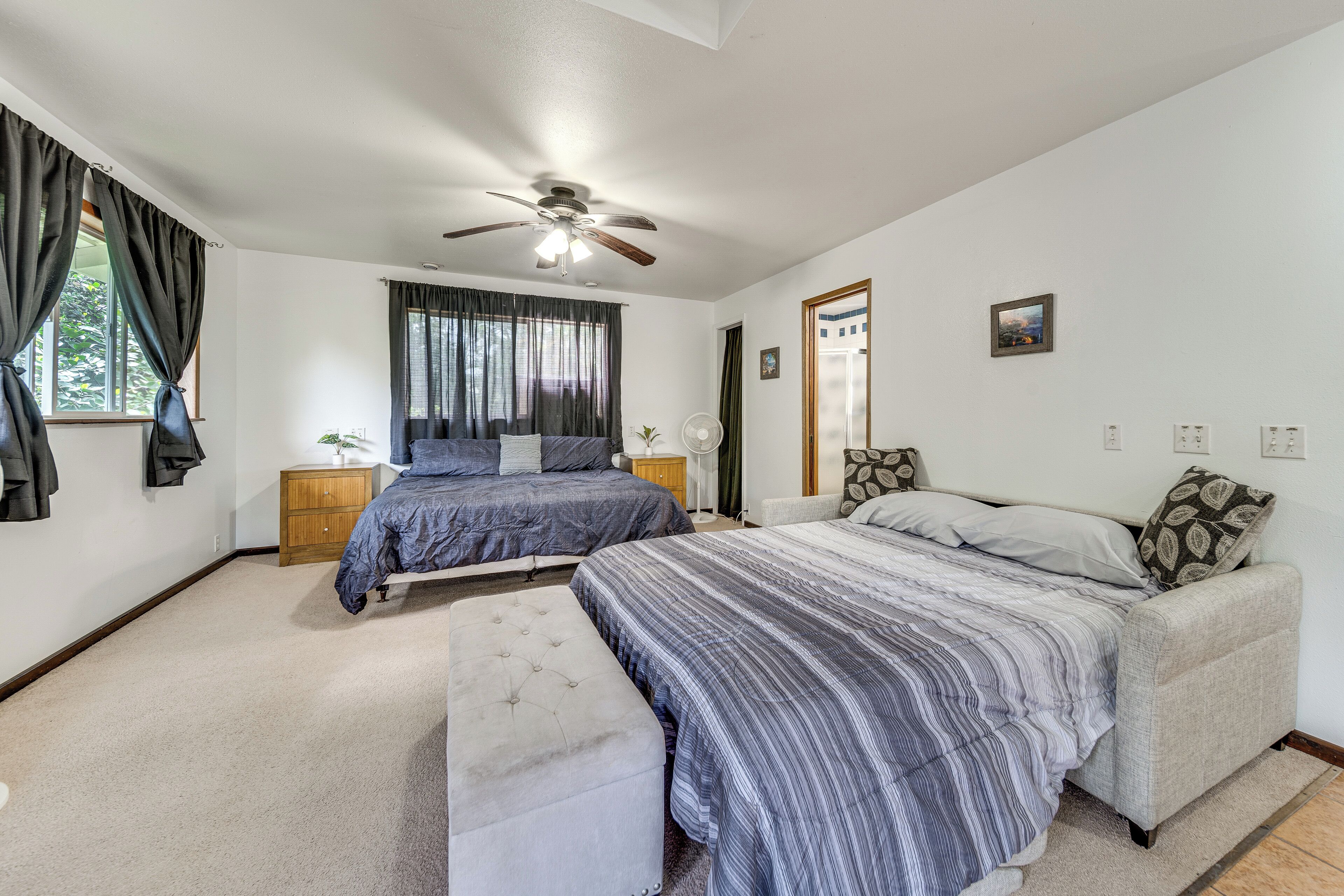 A bedroom with two beds, a ceiling fan, a window with curtains, a bedside table, and a small plant.