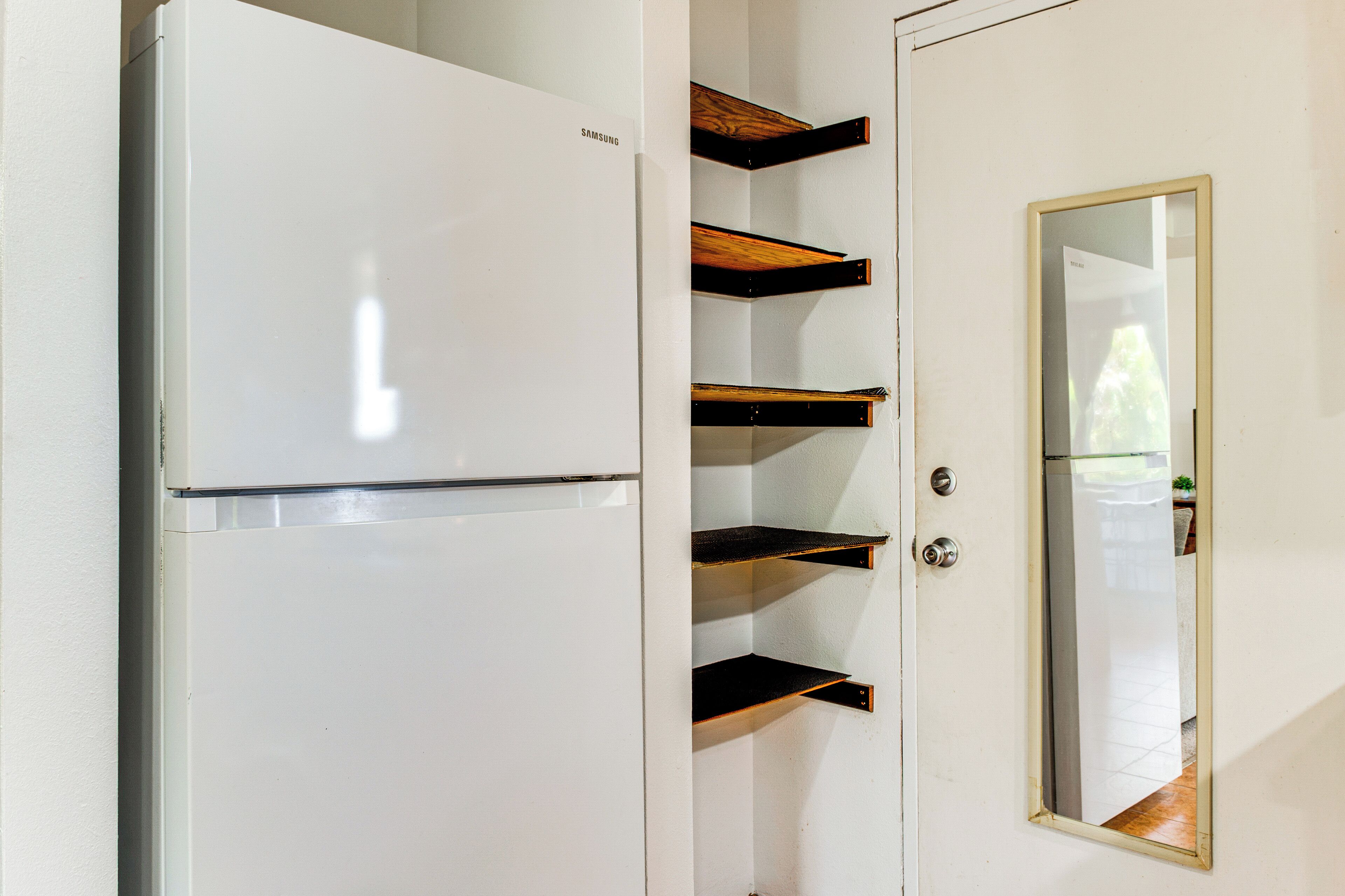 Un réfrigérateur blanc orné du logo Samsung, une étagère en bois et un miroir sur la porte.