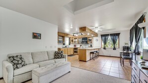 A spacious living room with a sofa and ottoman, a kitchen with wooden cabinets and a central island, and a dining area with a table and chairs. - 4 Mi to Beach: Keaau Retreat w/ Relaxing Porch! (Keaau)