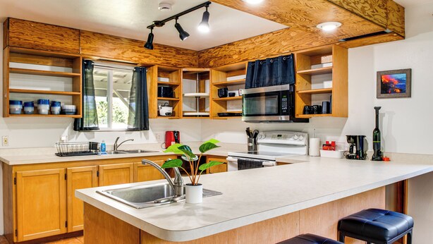 A modern kitchen with wooden cabinets, a central island with a sink, and built-in appliances. - 4 Mi to Beach: Keaau Retreat w/ Relaxing Porch! (Keaau)