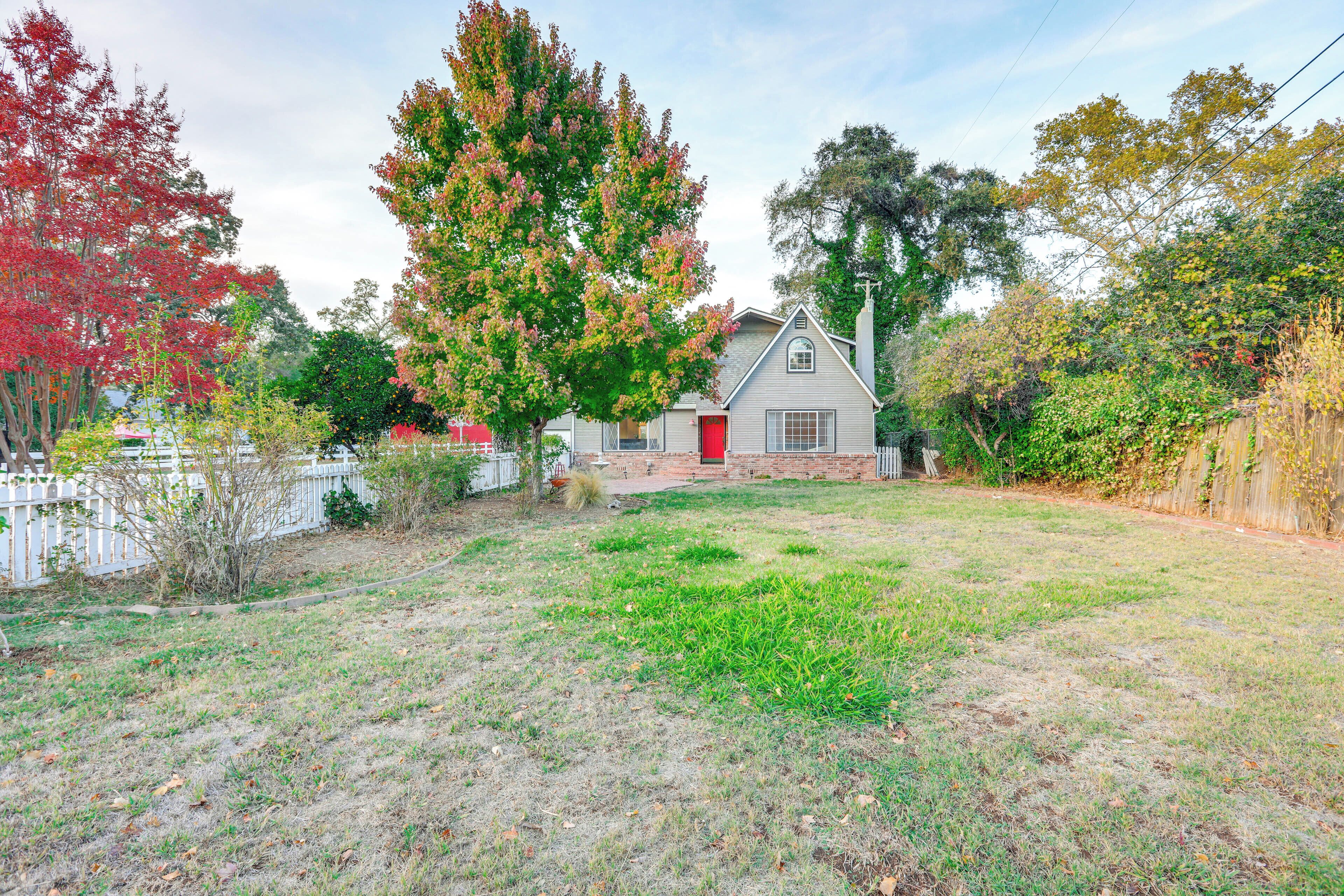 A house with a red door, surrounded by a white picket fence, and a grassy yard with trees in the background.