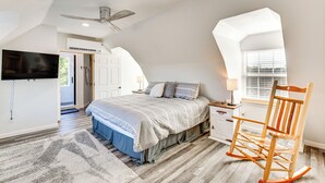 Ein Schlafzimmer mit einem Bett, einem Schaukelstuhl aus Holz, einem Fernseher und einem Fenster mit Jalousien.