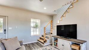Ein Wohnzimmer mit Treppe, Flachbildfernseher, Sofa und einem gemusterten Teppich.