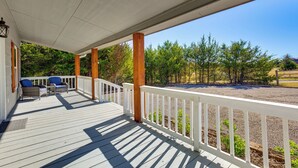 Eine überdachte Terrasse mit weißen Geländern, Holzbalken und zwei blauen Stühlen.