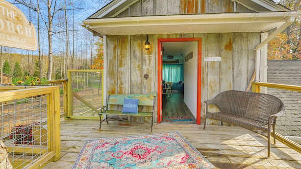 A rustic cabin with a wooden exterior, a porch with a bench and a rug, and a sign reading "The Porch". - Countryside Gem on Homestead in Asheboro! (Asheboro)