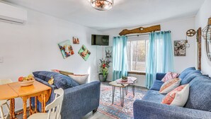 A living room with a sofa, chairs, a dining table with fruit, a TV, and artwork on the walls. - Countryside Gem on Homestead in Asheboro! (Asheboro)
