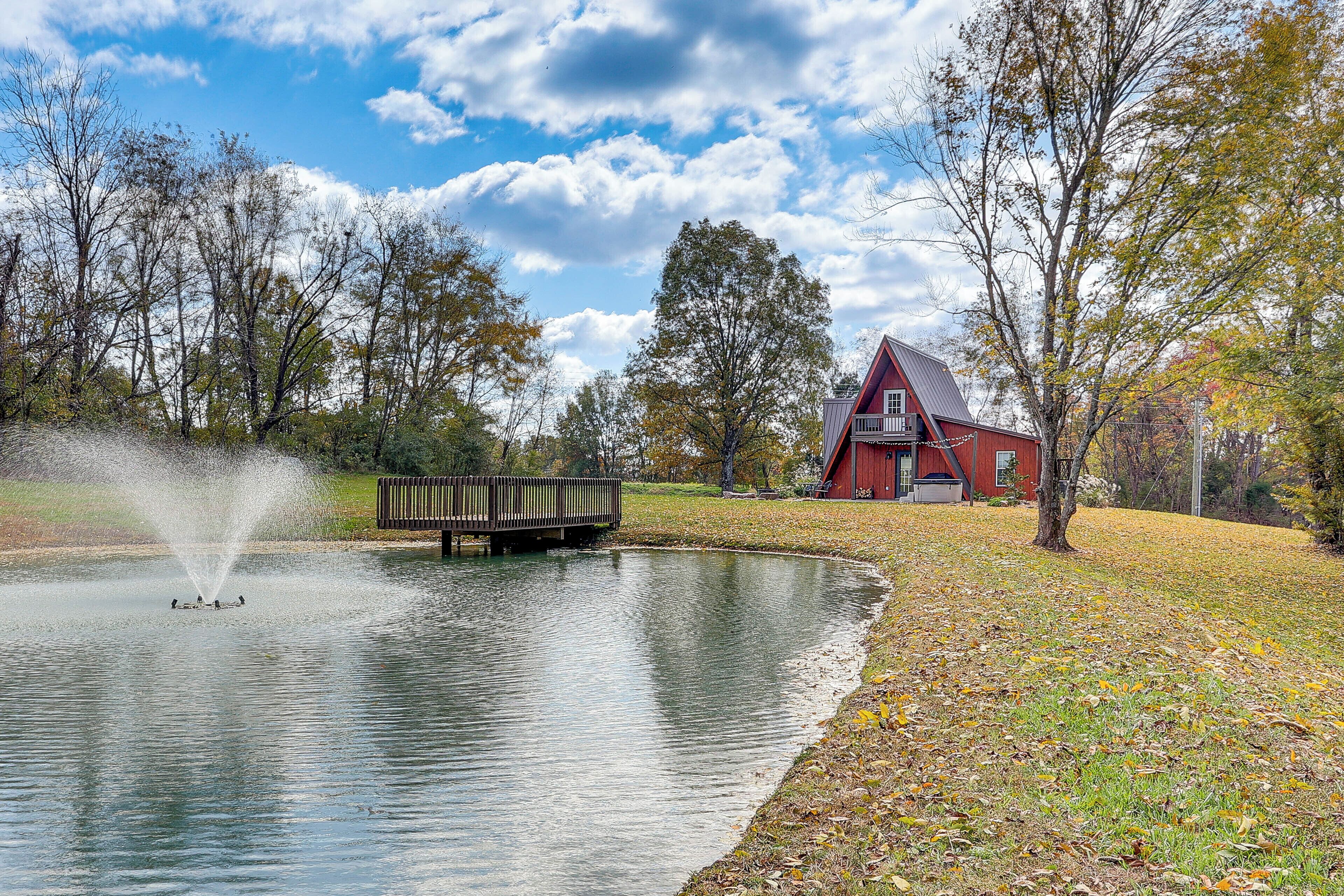 A pond with a fountain, surrounded by trees and a red barn.