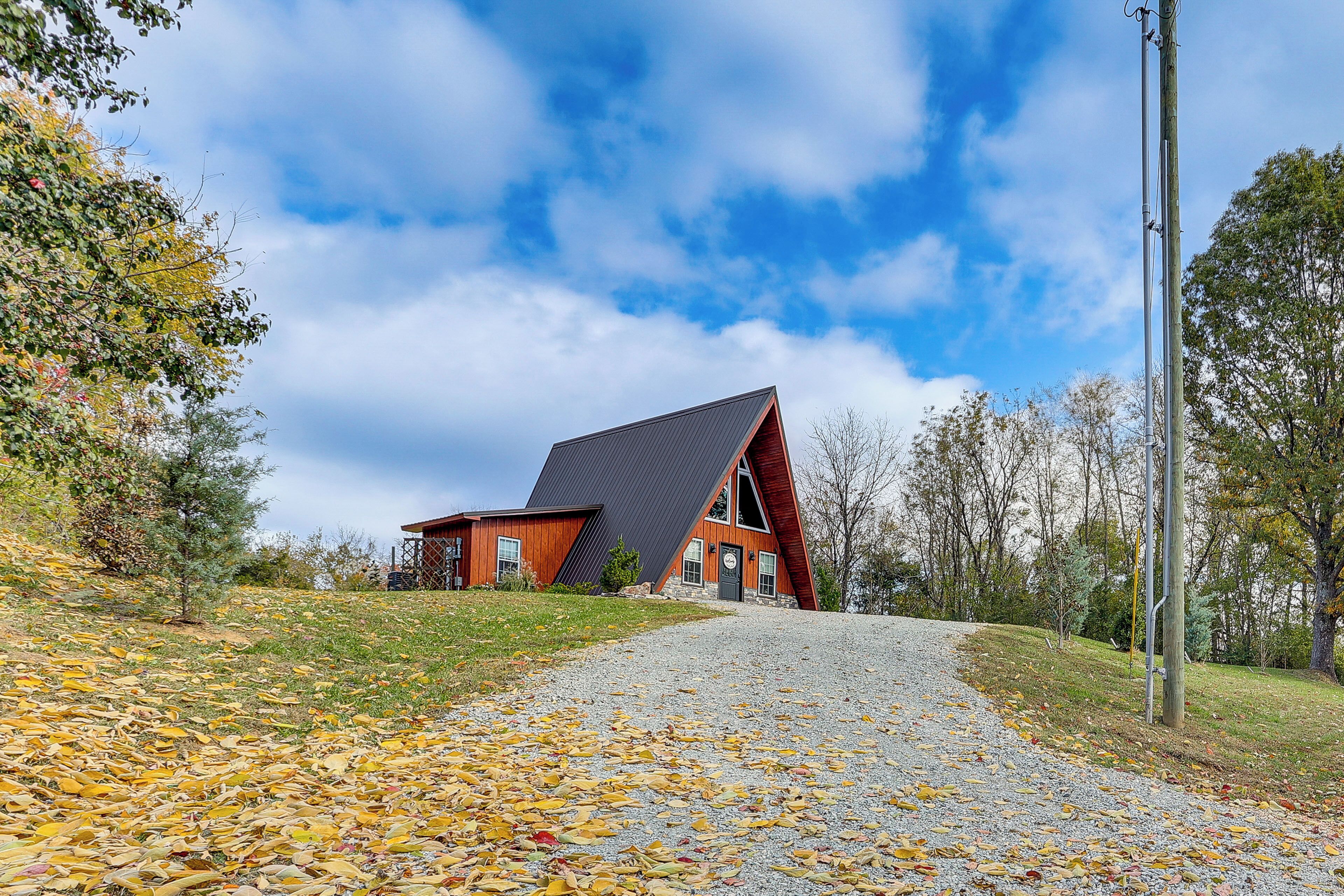A modern building with a sloped roof, situated on a gravel path surrounded by trees and autumn leaves.