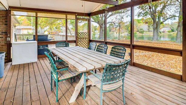 A covered patio with a wooden table and chairs, large windows, and a view of a lake and trees. - Screened Patio, Deck & Grill: Saint Inigoes Home! (Saint Inigoes)
