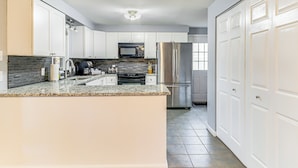 A modern kitchen with white cabinets, a granite countertop, stainless steel appliances, and a tiled floor. - Screened Patio, Deck & Grill: Saint Inigoes Home! (Saint Inigoes)