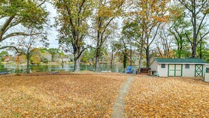 A backyard with a paved path, a small shed, and a fenced area with trees and a body of water in the background. - Screened Patio, Deck & Grill: Saint Inigoes Home! (Saint Inigoes)