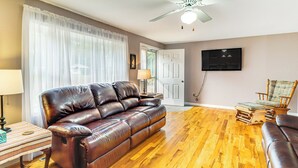 A living room with a leather sofa, wooden flooring, a ceiling fan, a TV, and a chair. - Screened Patio, Deck & Grill: Saint Inigoes Home! (Saint Inigoes)