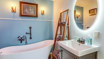 A bathroom with a freestanding bathtub, a vanity with a mirror, and wall-mounted lighting.
