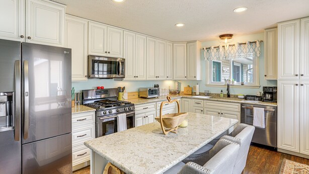 A modern kitchen with white cabinetry, stainless steel appliances, a granite countertop, and a central island with seating. - Walk to Sandusky Bay: Home w/ Hot Tub & Fire Pit! (Sandusky)
