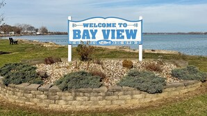 A welcome sign to Bay View with a view of a lake and a grassy area with a bench. - Walk to Sandusky Bay: Home w/ Hot Tub & Fire Pit! (Sandusky)