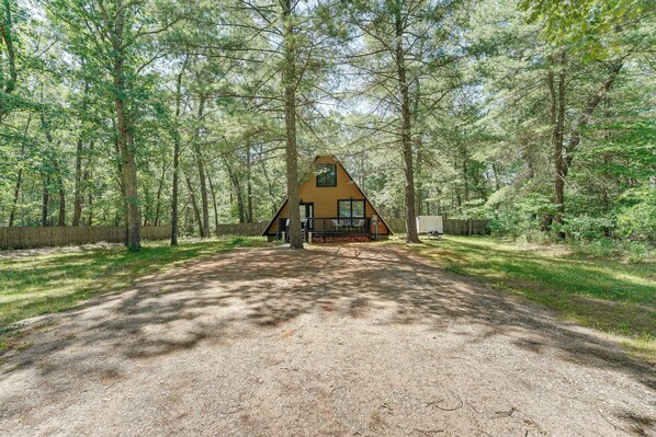 A cabin in a forest with a gravel driveway leading to it.