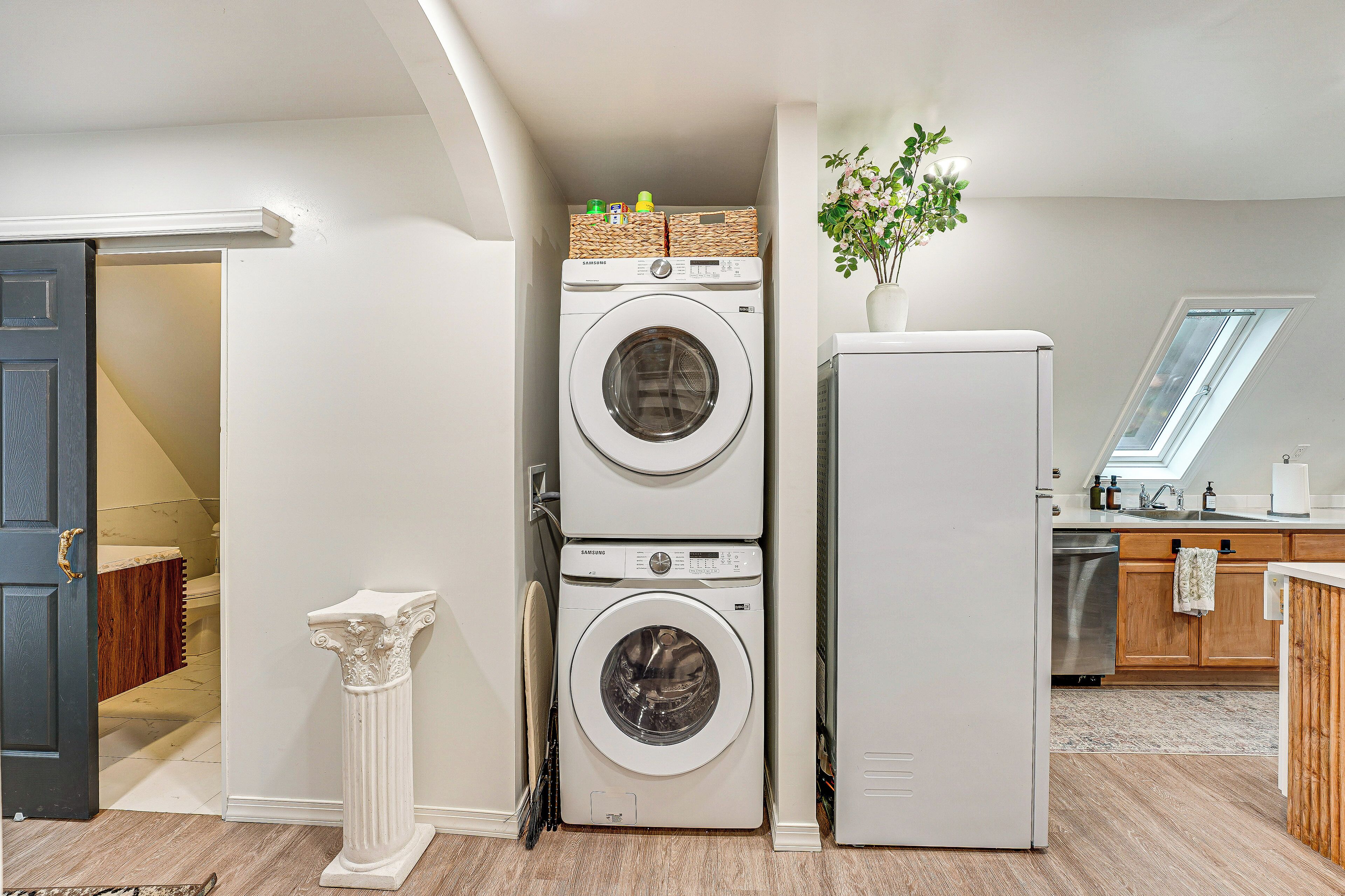 A laundry room with stacked washers and dryers, a white pillar, and a plant.