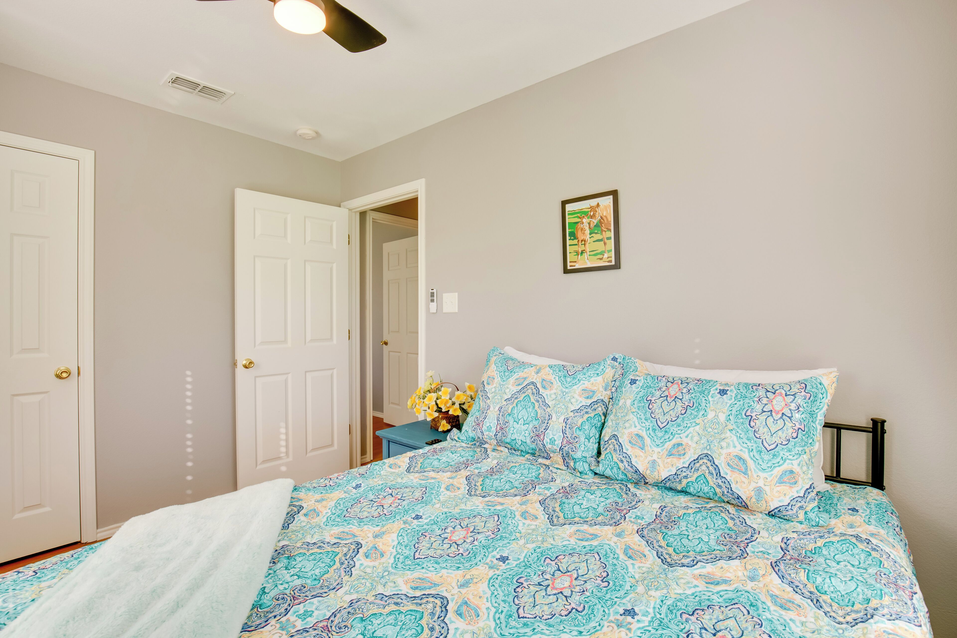 A bedroom with a patterned bedspread, a ceiling fan, and a door leading to another room.