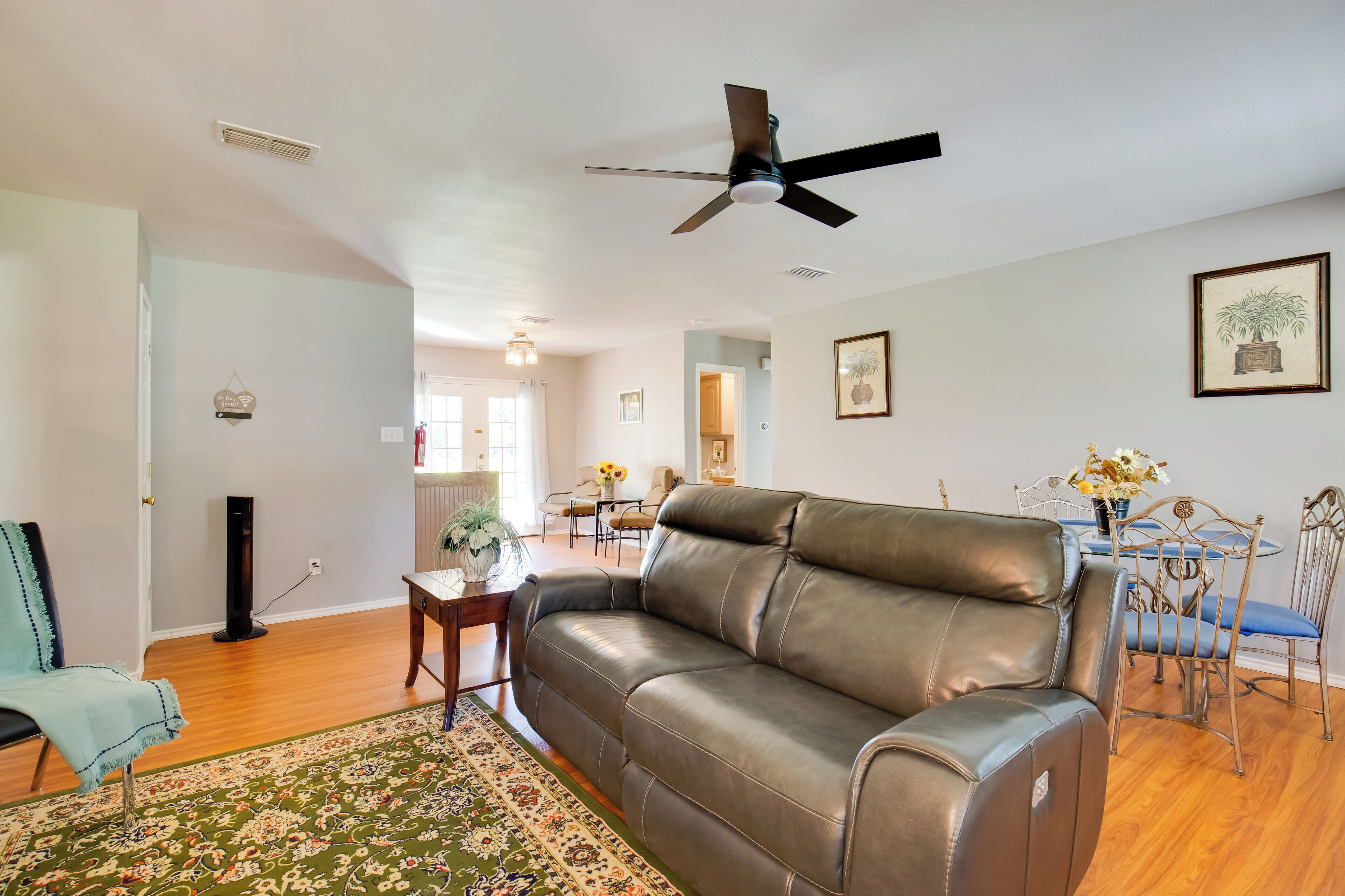 A living room with a leather sofa, a dining table with chairs, a ceiling fan, and a patterned rug.