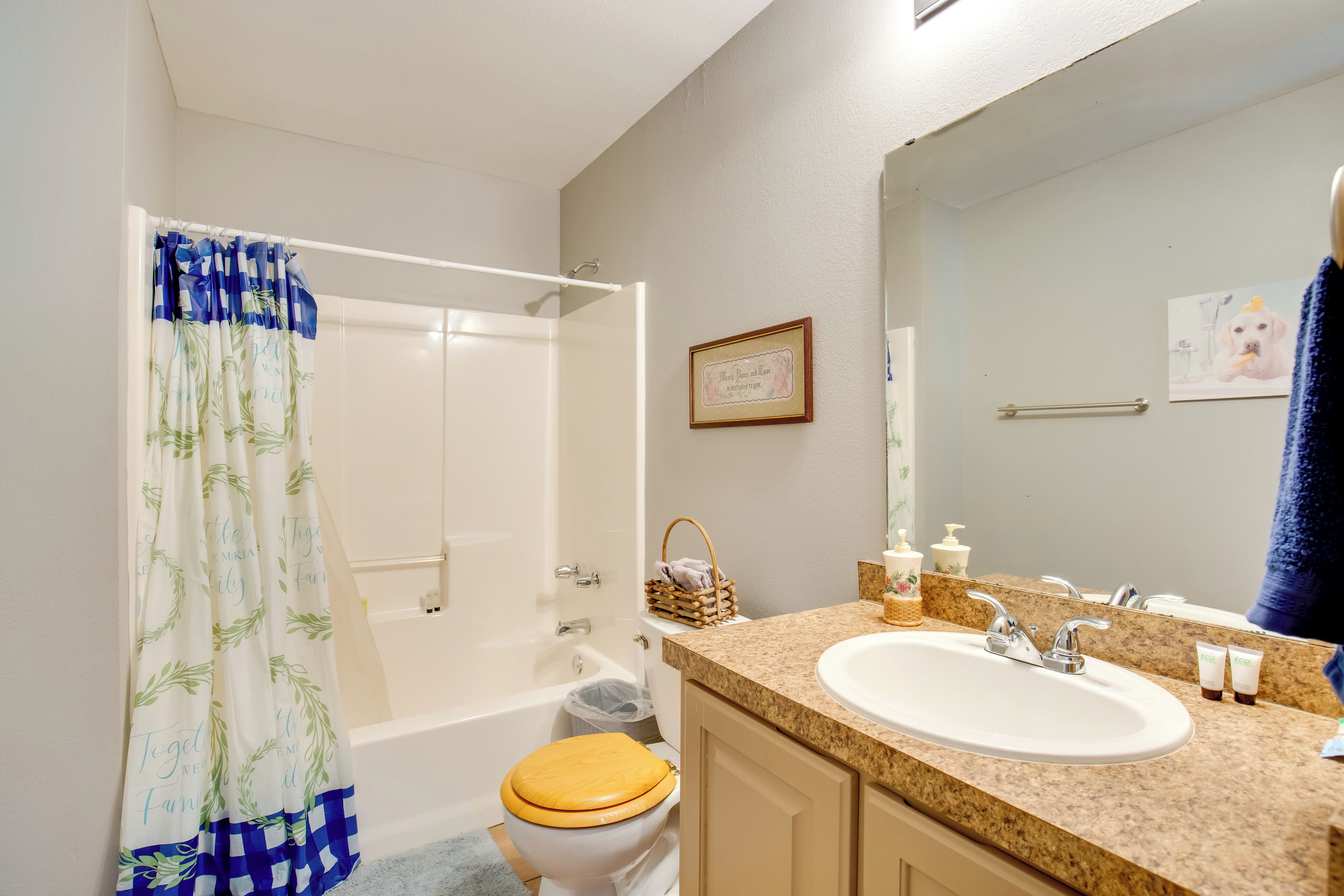 A bathroom with a shower curtain, toilet, bathtub, sink, and a framed picture on the wall.