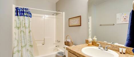 A bathroom with a shower curtain, toilet, bathtub, sink, and a framed picture on the wall.