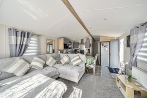 Una sala de estar moderna y bien iluminada con un sofá, una mesa de comedor y una zona de cocina al fondo.