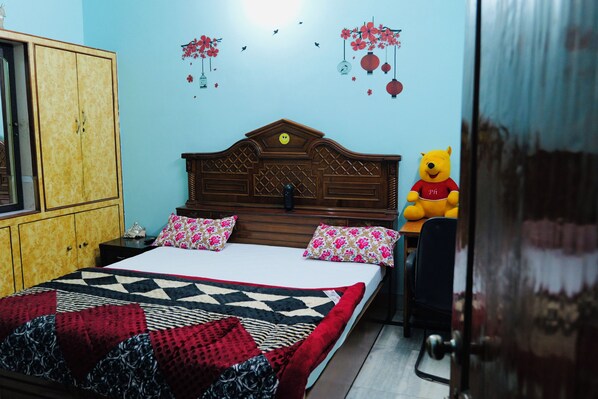 A bedroom with a wooden bed, two pillows, a red and black quilt, a wooden wardrobe, and a Winnie the Pooh plush toy.