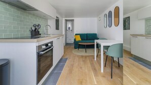 Eine kompakte Küche mit einer zentralen Kochinsel, ein Essbereich mit Tisch und Stühlen sowie ein Wohnbereich mit Sofa und Kissen.