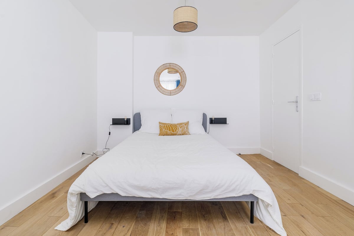Un dormitorio con cama, mesita de noche, lámpara, espejo y puerta.