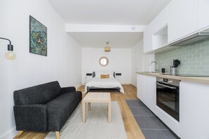 A compact living space with a bed, a sofa, a small table, a kitchen area with a stove, and a wall-mounted mirror. - BRIDGESTREET LE MARAIS LES HALLES (Paris)