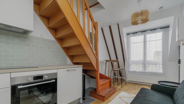 Eine moderne Küche mit einer Holztreppe, einem Essbereich mit Tisch und Stühlen sowie einem großen Fenster mit Aussicht.
