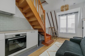 A modern kitchen with a wooden staircase, a dining area with a table and chairs, and a large window with a view. - BRIDGESTREET LE MARAIS LES HALLES (Paris)