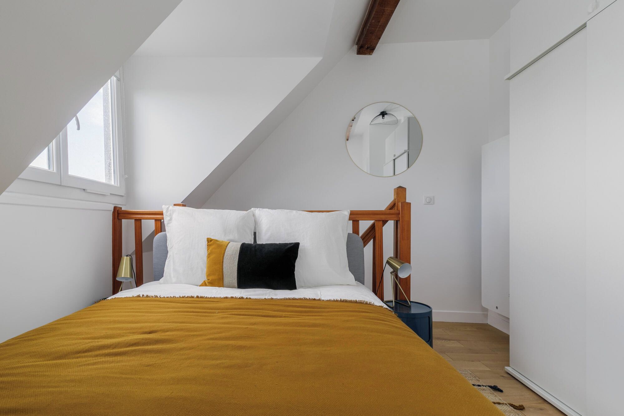 A bedroom with a sloped ceiling, a bed with a mustard-colored blanket, white pillows, and a wooden headboard.