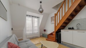 Ein modernes Apartment mit einer offenen Wohnküche, einer Holztreppe und einem gemütlichen Wohnbereich mit Sofa und kleinem Tisch.