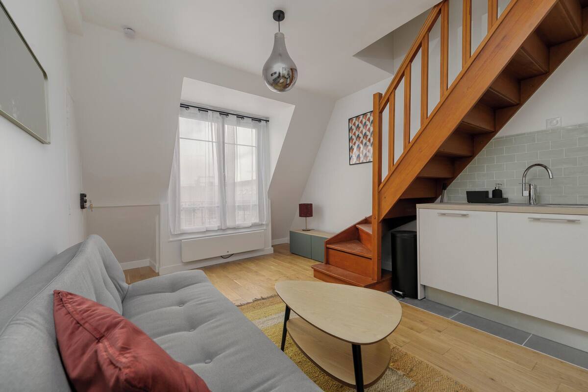 Un apartamento moderno con cocina tipo loft, una escalera de madera y una zona de estar acogedora con un sofá y una pequeña mesa.
