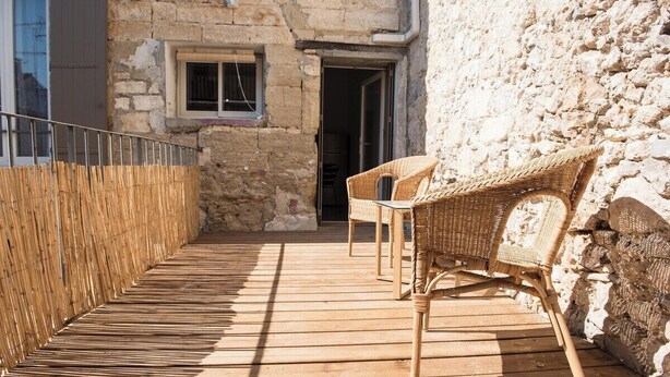 A wooden deck with wicker furniture, stone walls, and a metal railing.
