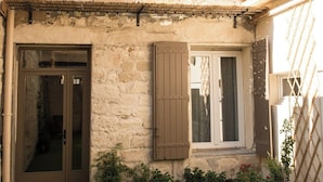 A stone building with a front door, two windows with shutters, and a small balcony.