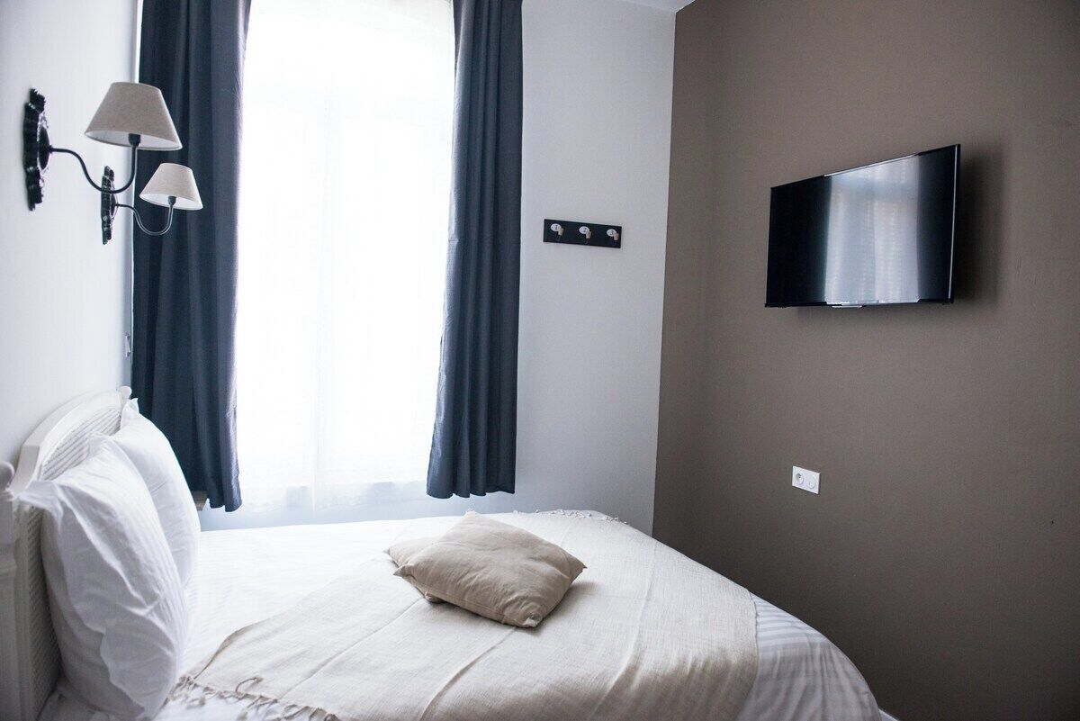 Une chambre d’hôtel avec un lit, un téléviseur fixé au mur et une fenêtre avec des rideaux.